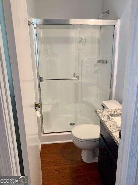 full bath featuring a shower stall, toilet, vanity, and wood finished floors