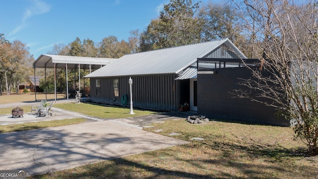 view of side of property featuring an outdoor fire pit, a yard, concrete driveway, metal roof, and a carport