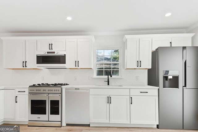 kitchen featuring a sink, stainless steel appliances, light countertops, white cabinets, and crown molding