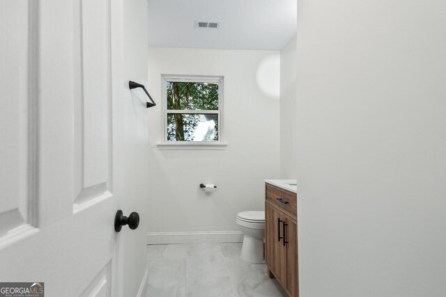 half bath with visible vents, vanity, marble finish floor, toilet, and baseboards