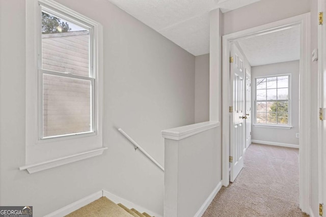hall with a textured ceiling, carpet flooring, baseboards, and an upstairs landing