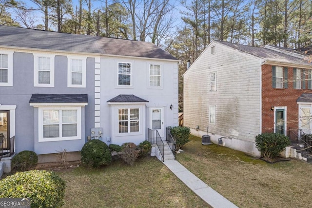 view of front of house with stucco siding, central AC unit, and a front lawn