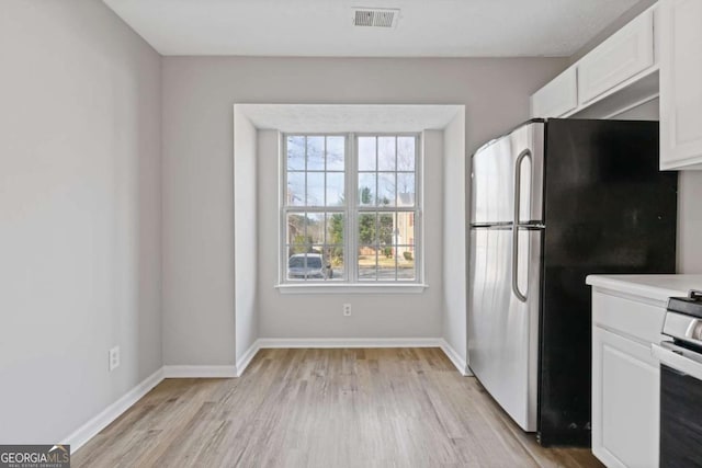 kitchen with freestanding refrigerator, white cabinets, visible vents, light wood finished floors, and baseboards