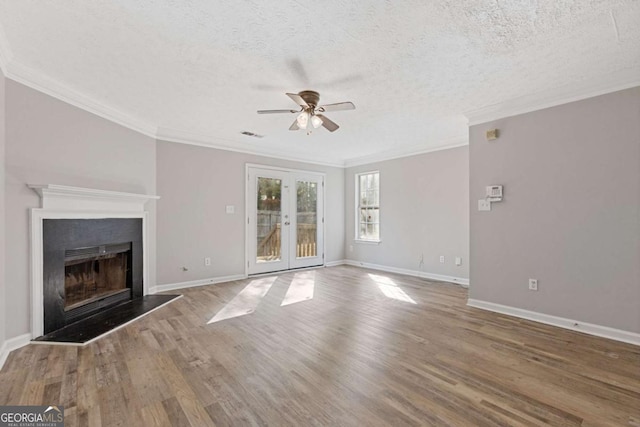 unfurnished living room featuring ceiling fan, ornamental molding, a fireplace with raised hearth, wood finished floors, and french doors