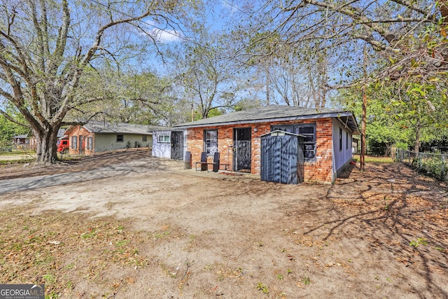 view of front of house featuring an outbuilding, fence, brick siding, and dirt driveway