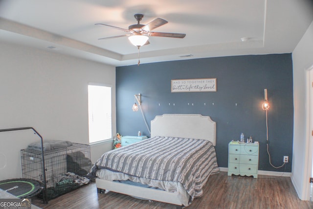 bedroom with wood finished floors, baseboards, visible vents, a tray ceiling, and ceiling fan