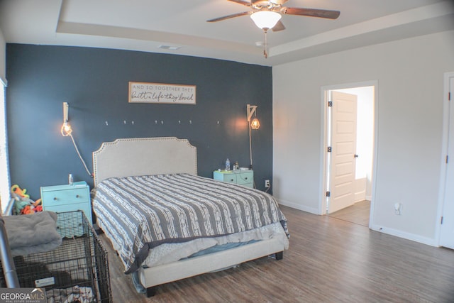 bedroom featuring ensuite bath, a tray ceiling, wood finished floors, and baseboards