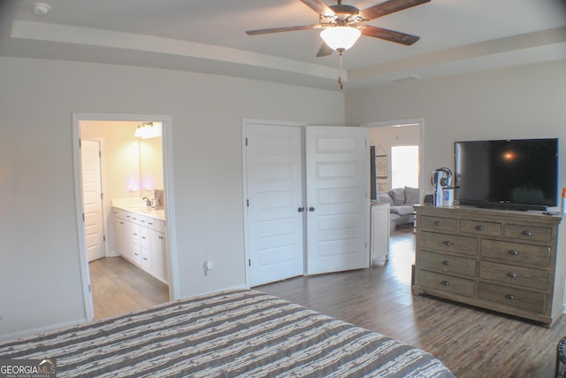 bedroom with a sink, connected bathroom, a raised ceiling, and wood finished floors