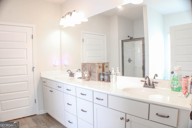 bathroom featuring double vanity, wood finished floors, a stall shower, and a sink