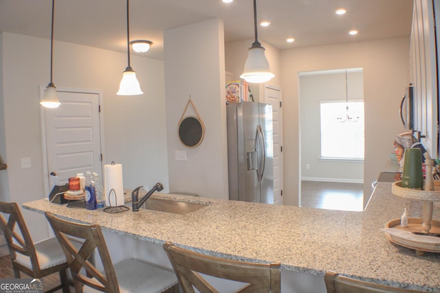 kitchen featuring light stone countertops, a breakfast bar area, recessed lighting, stainless steel fridge, and a sink