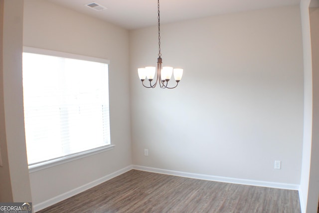 empty room featuring an inviting chandelier, wood finished floors, visible vents, and baseboards