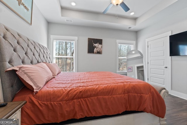 bedroom with visible vents, baseboards, a tray ceiling, and wood finished floors