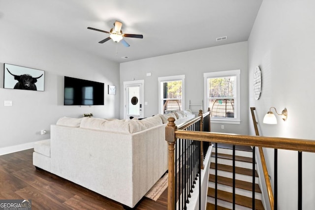 living room featuring a ceiling fan, dark wood-style floors, visible vents, and baseboards