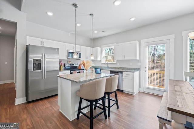 kitchen featuring light stone counters, a center island, white cabinetry, appliances with stainless steel finishes, and a healthy amount of sunlight