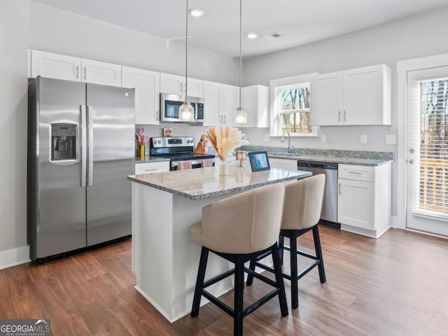 kitchen featuring light stone counters, appliances with stainless steel finishes, white cabinetry, and a sink