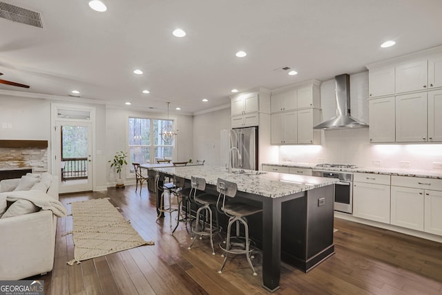 kitchen featuring visible vents, open floor plan, an island with sink, stainless steel appliances, and wall chimney exhaust hood