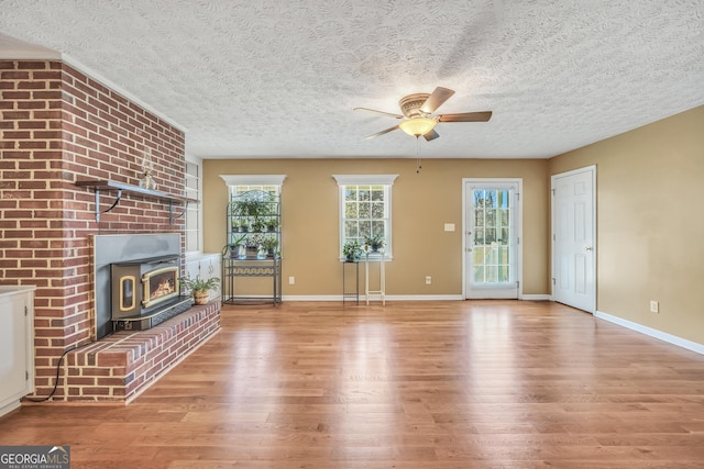 unfurnished living room with wood finished floors, baseboards, a wood stove, ceiling fan, and a textured ceiling