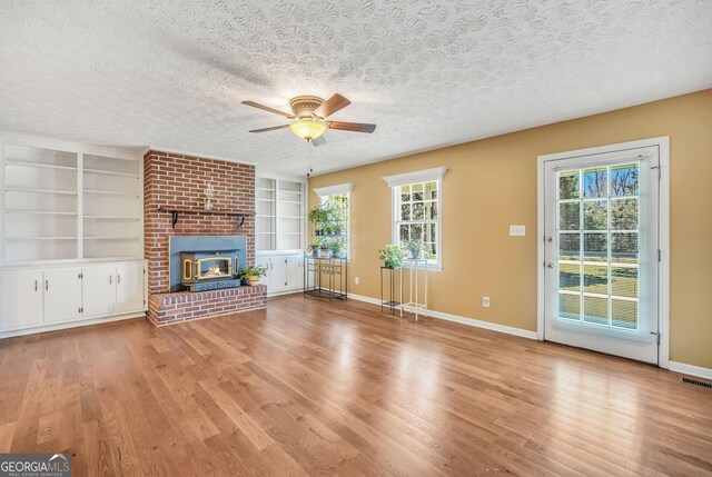unfurnished living room featuring visible vents, built in shelves, a textured ceiling, wood finished floors, and a fireplace