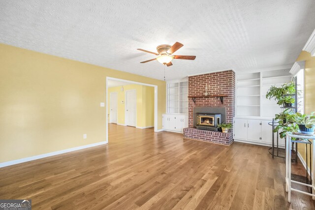 unfurnished living room with built in features, a textured ceiling, and wood finished floors