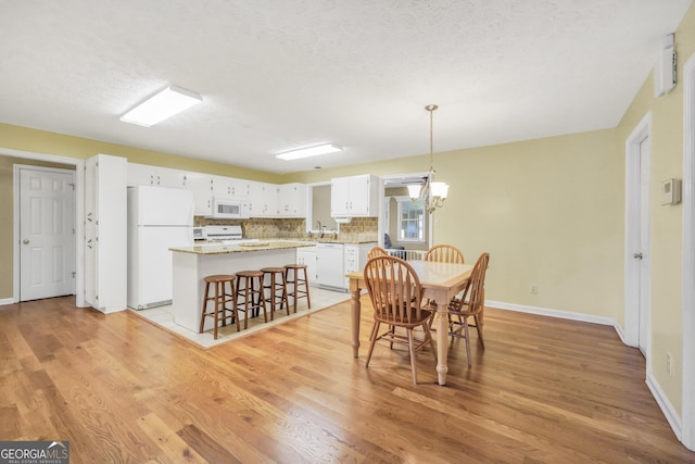 dining room featuring an inviting chandelier, baseboards, light wood finished floors, and a textured ceiling