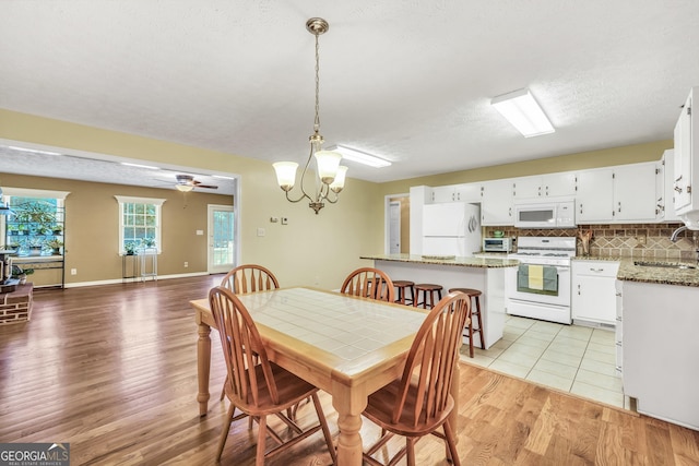 dining room featuring baseboards, a toaster, a textured ceiling, ceiling fan with notable chandelier, and light wood-type flooring