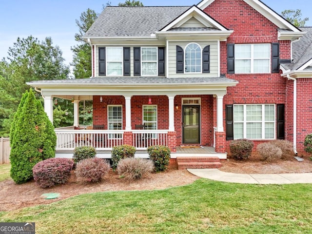 view of front of property featuring brick siding, a porch, a front lawn, and roof with shingles