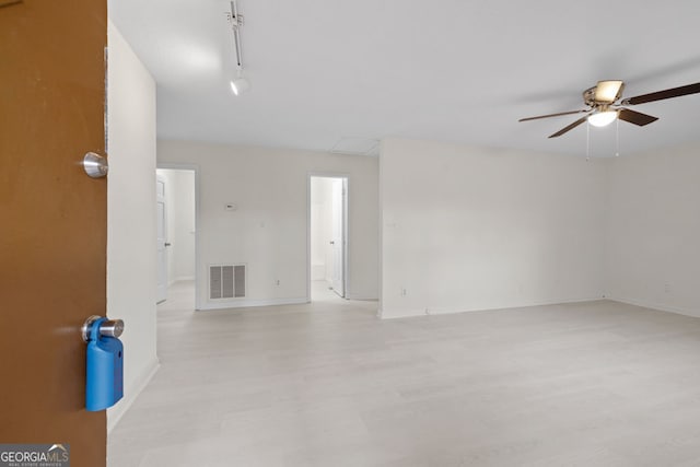 empty room featuring visible vents, light wood-style flooring, rail lighting, baseboards, and ceiling fan