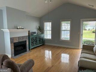 living area with wood finished floors, a fireplace, baseboards, and lofted ceiling