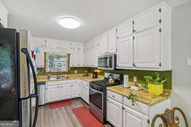 kitchen with white cabinets, wood finished floors, appliances with stainless steel finishes, and a sink