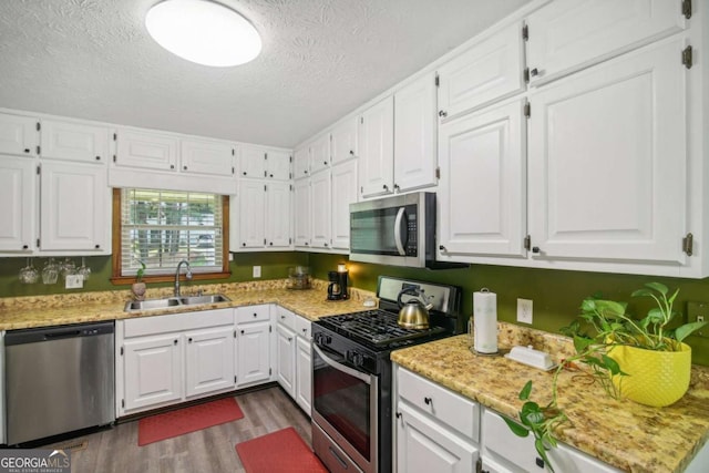 kitchen with dark wood finished floors, a sink, stainless steel appliances, white cabinets, and a textured ceiling