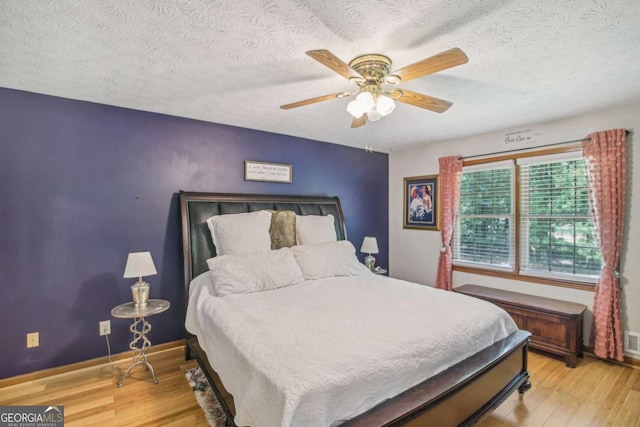 bedroom featuring ceiling fan, baseboards, a textured ceiling, and wood finished floors