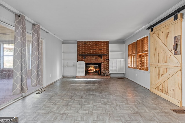 unfurnished living room with baseboards, visible vents, ornamental molding, a barn door, and a brick fireplace