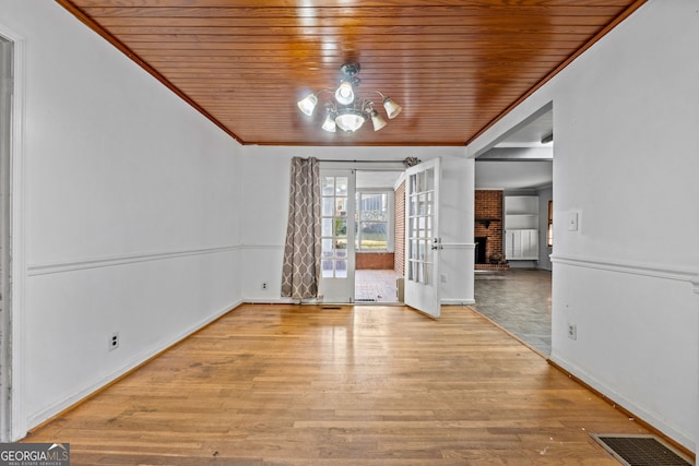 interior space with visible vents, a brick fireplace, ornamental molding, wooden ceiling, and wood finished floors