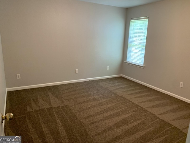 spare room featuring baseboards and dark carpet