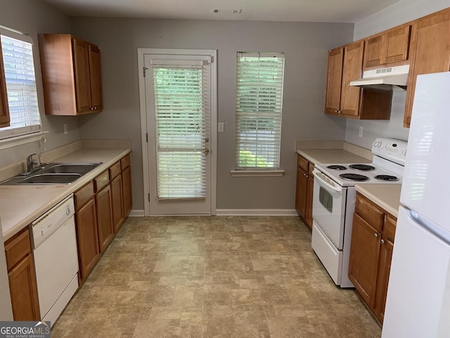 kitchen with a sink, white appliances, under cabinet range hood, and brown cabinets