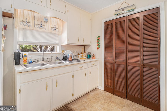 kitchen with a sink, backsplash, crown molding, and light countertops