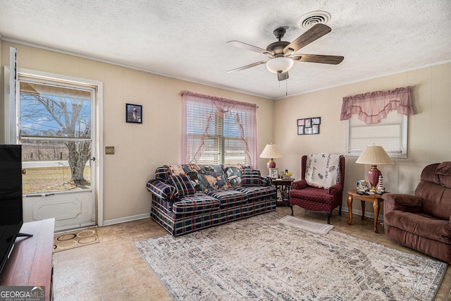 living room featuring visible vents, ornamental molding, a textured ceiling, baseboards, and ceiling fan