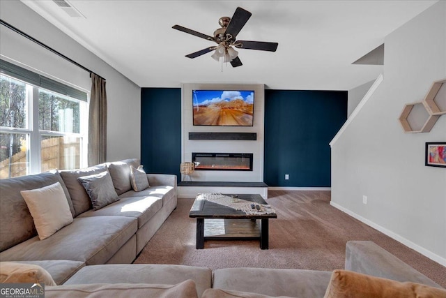 carpeted living area with a glass covered fireplace, visible vents, baseboards, and a ceiling fan