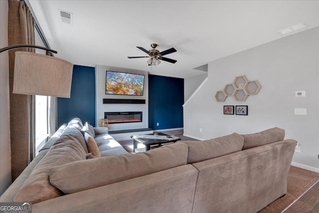 living area featuring a glass covered fireplace, visible vents, baseboards, and ceiling fan