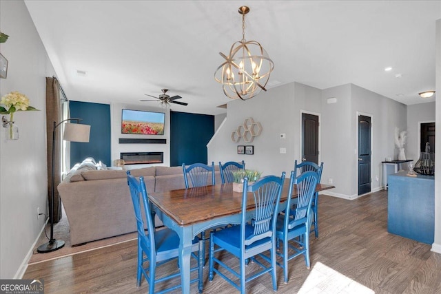 dining area with a glass covered fireplace, ceiling fan with notable chandelier, baseboards, and wood finished floors