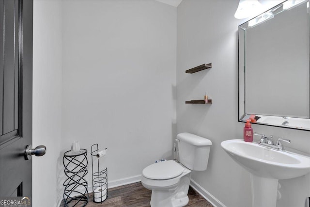 bathroom with toilet, wood finished floors, baseboards, and a sink