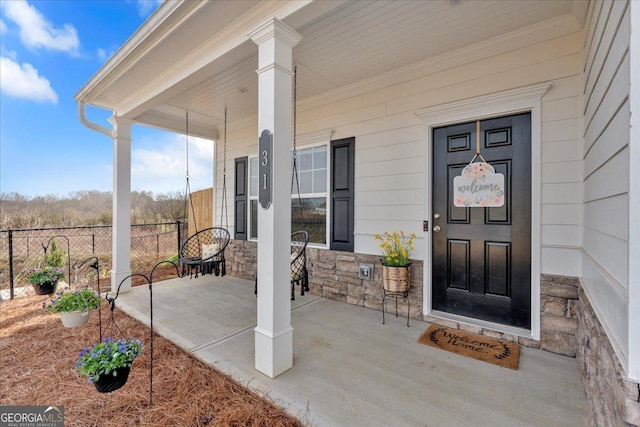 view of exterior entry with stone siding, covered porch, and fence