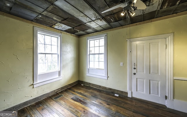 unfurnished room featuring a wealth of natural light, visible vents, dark wood-type flooring, and a ceiling fan