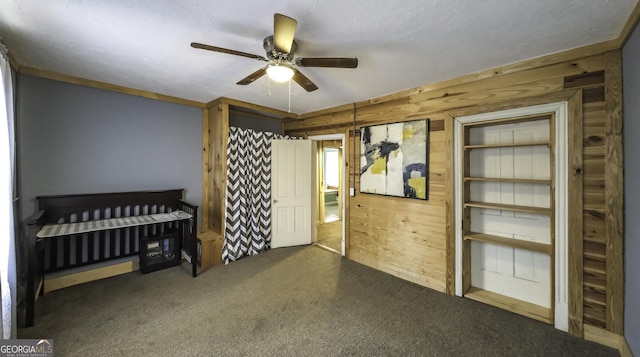 carpeted bedroom with wooden walls, a ceiling fan, and a textured ceiling