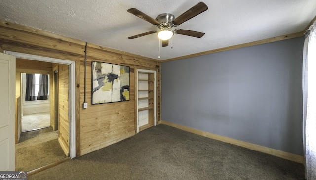 unfurnished room featuring wooden walls, a textured ceiling, baseboards, and dark colored carpet