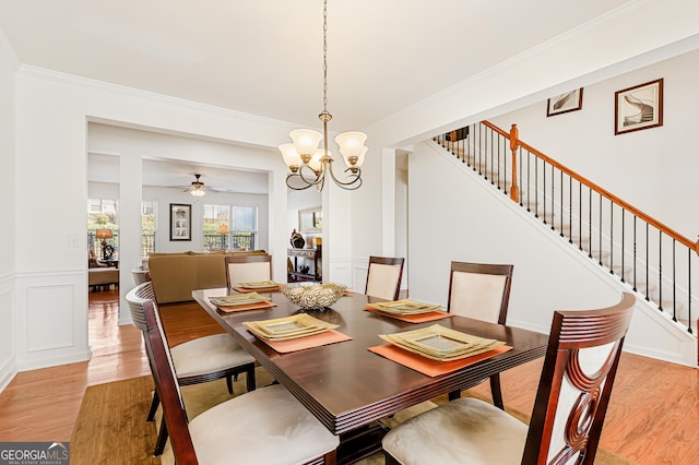 dining room with light wood finished floors, ornamental molding, stairway, wainscoting, and a decorative wall