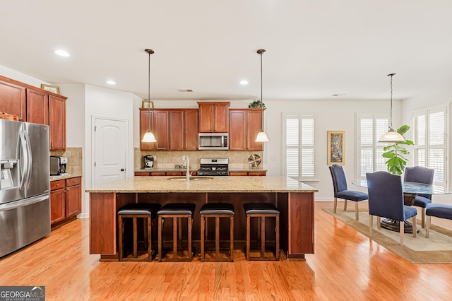 kitchen with hanging light fixtures, light wood finished floors, and appliances with stainless steel finishes