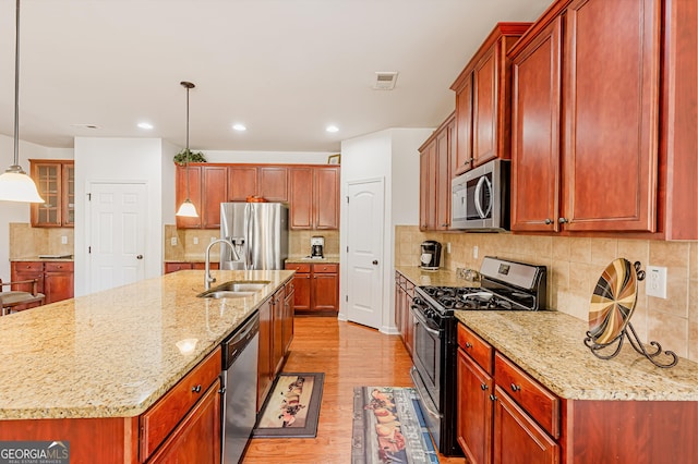 kitchen featuring a sink, stainless steel appliances, light stone countertops, and light wood finished floors