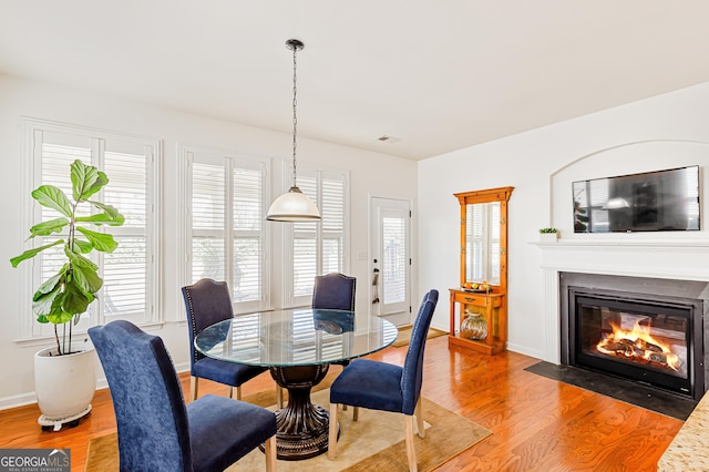 dining room with a fireplace with flush hearth, light wood-style flooring, visible vents, and baseboards