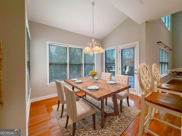 dining area featuring a chandelier, light wood-style flooring, high vaulted ceiling, and baseboards